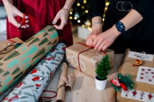 Two people wrapping several Christmas gifts. 