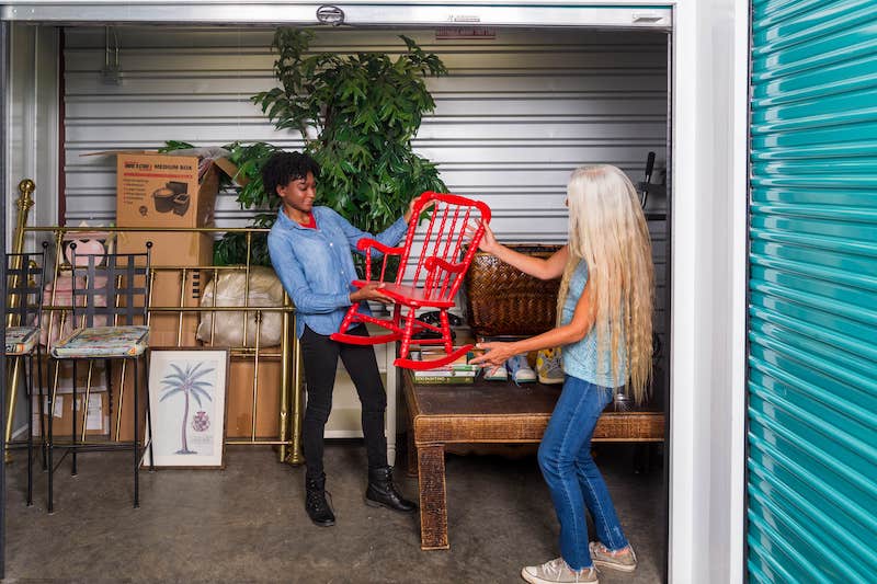 Two women holding up a chair in a storage unit.