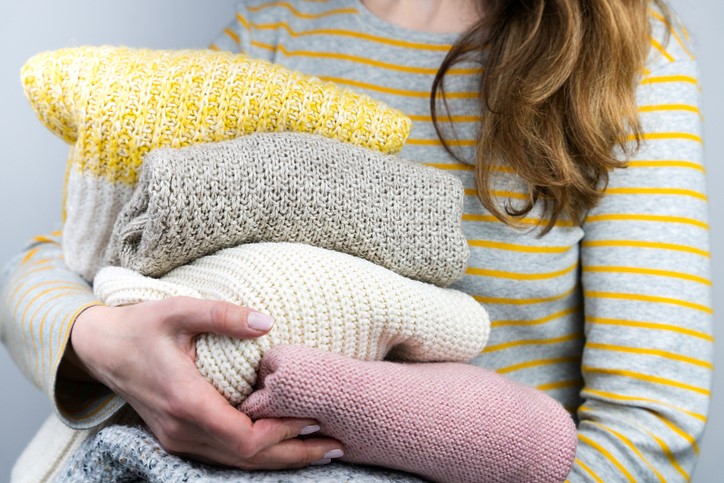 A woman holding knitted sweaters in preparation for organizing them.